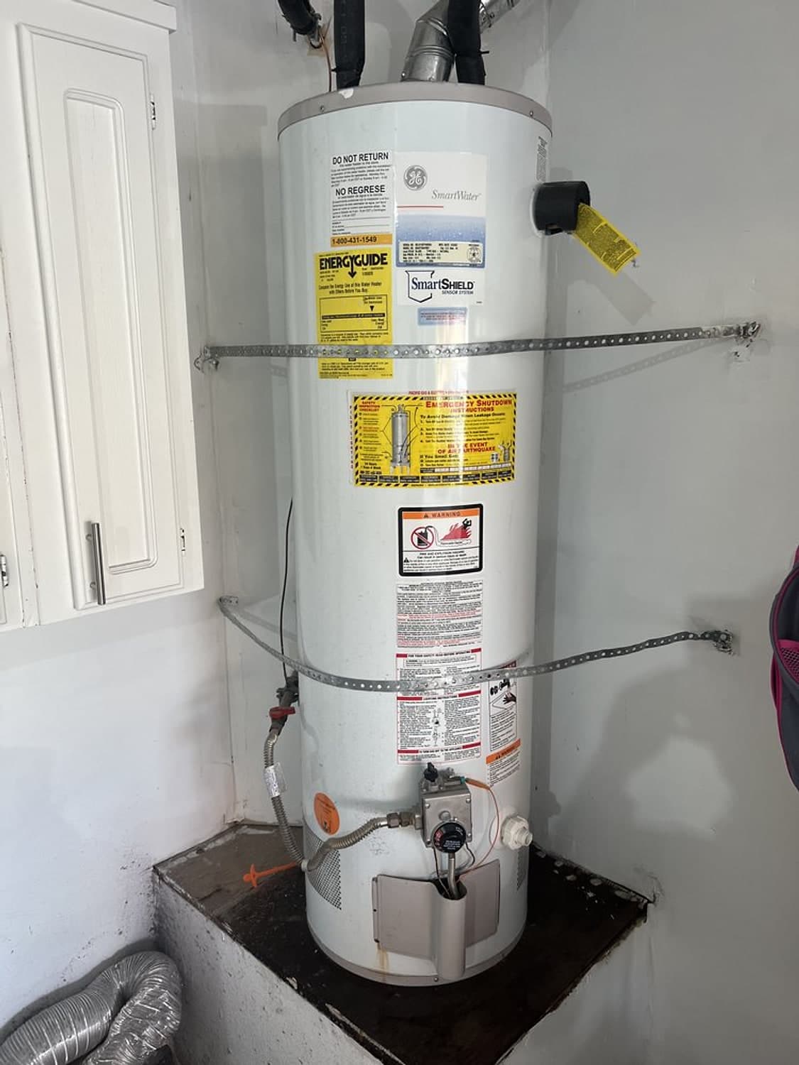 New 40-gallon tank water heater with seismic straps, set on a stand in a utility closet