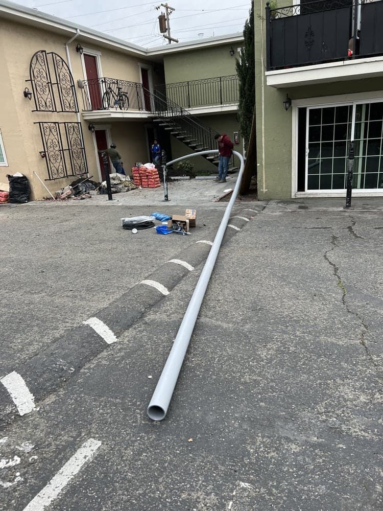 Long white PVC pipe laid across an apartment complex parking lot, crew and materials in the background