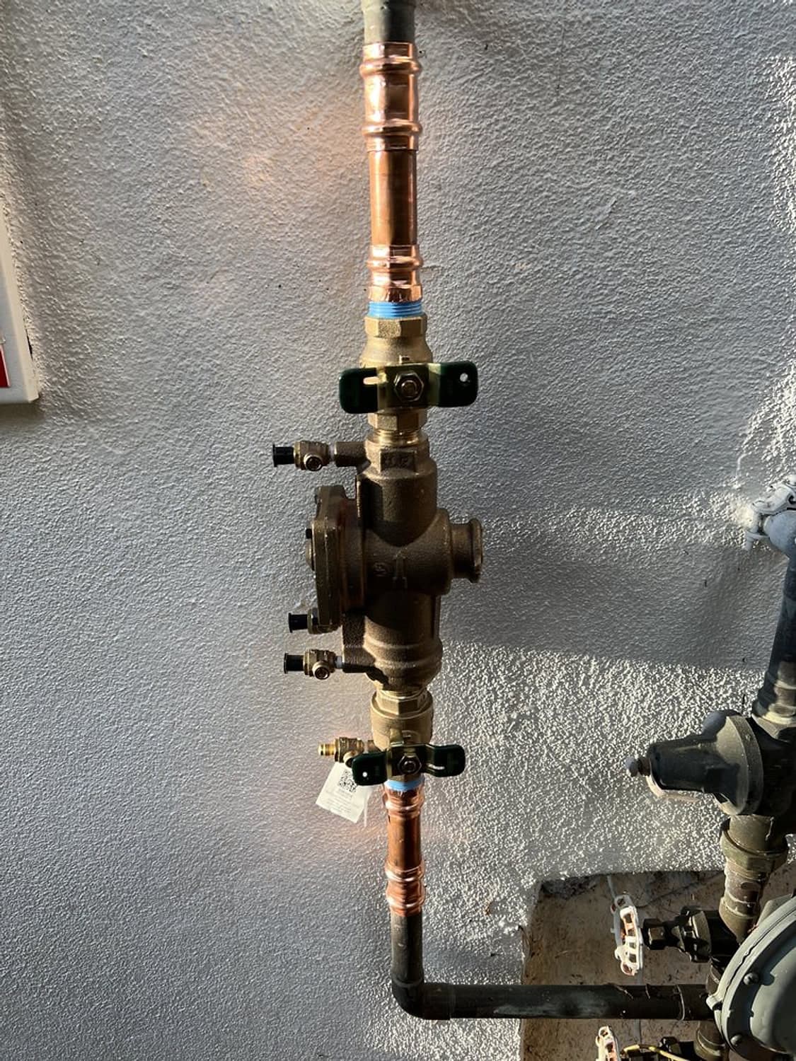 New brass backflow valve assembly installed on a copper water line against a white stucco wall