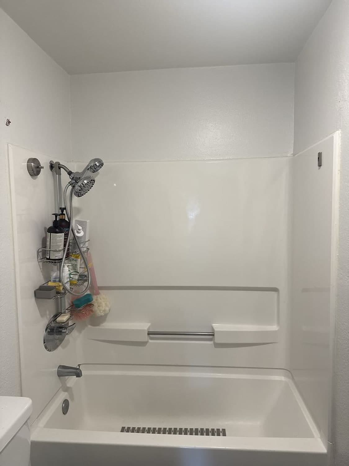 New white bathtub and shower walls with a chrome shower head and grab bar, during a bathroom remodel