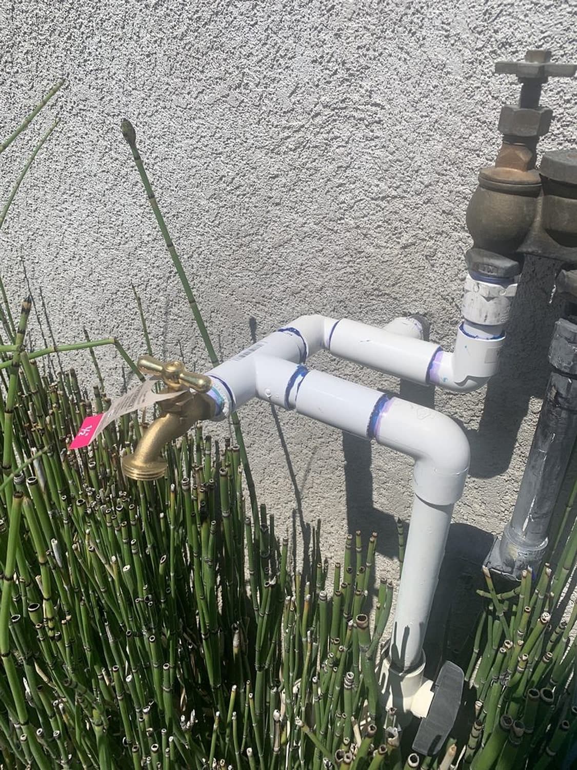 The same spot after the repair: new white pipe and fittings with a brass hose bib against the house wall