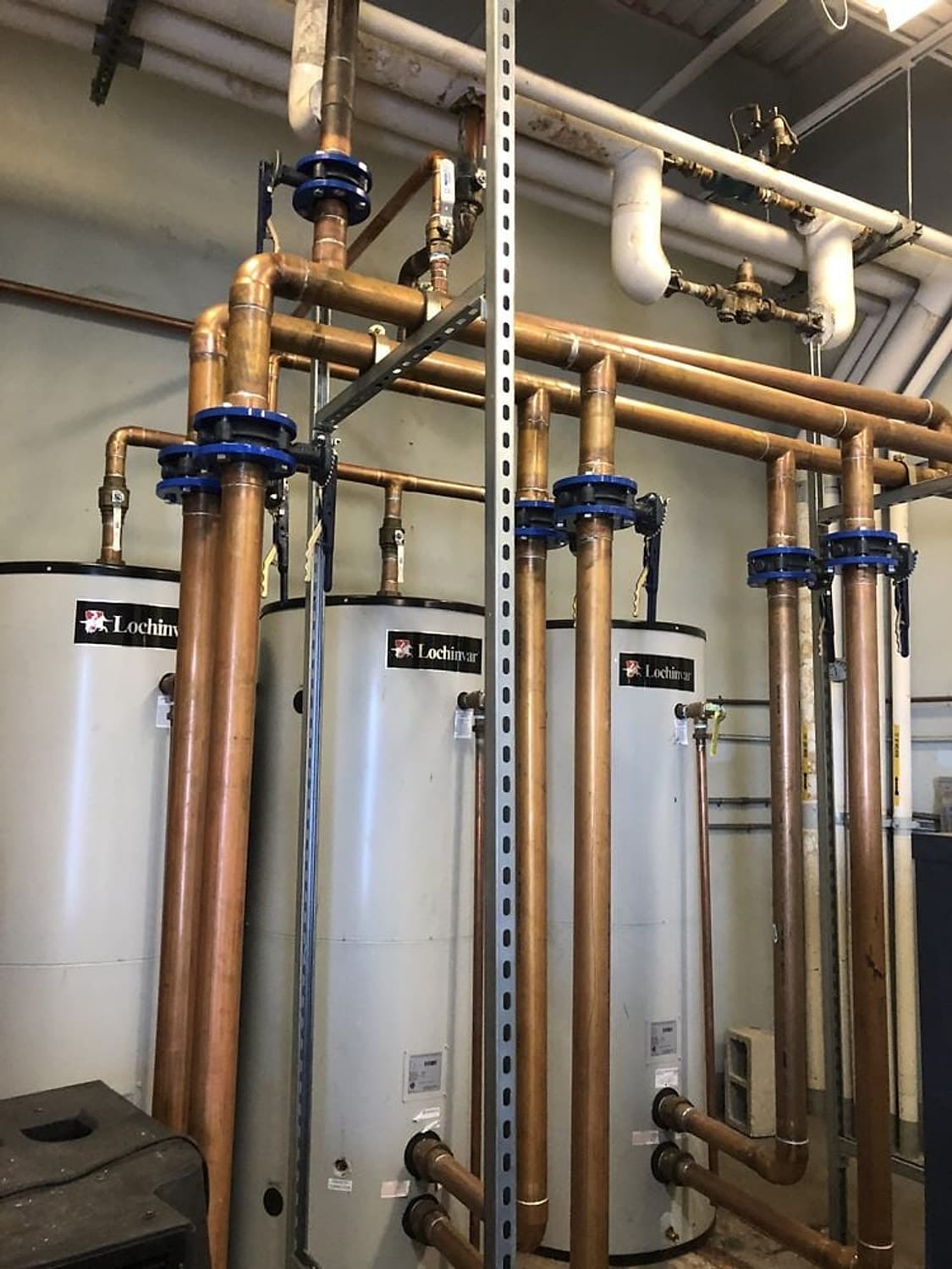 Tres calentadores de agua comerciales Lochinvar conectados con tubería de cobre y válvulas azules en un cuarto de máquinas