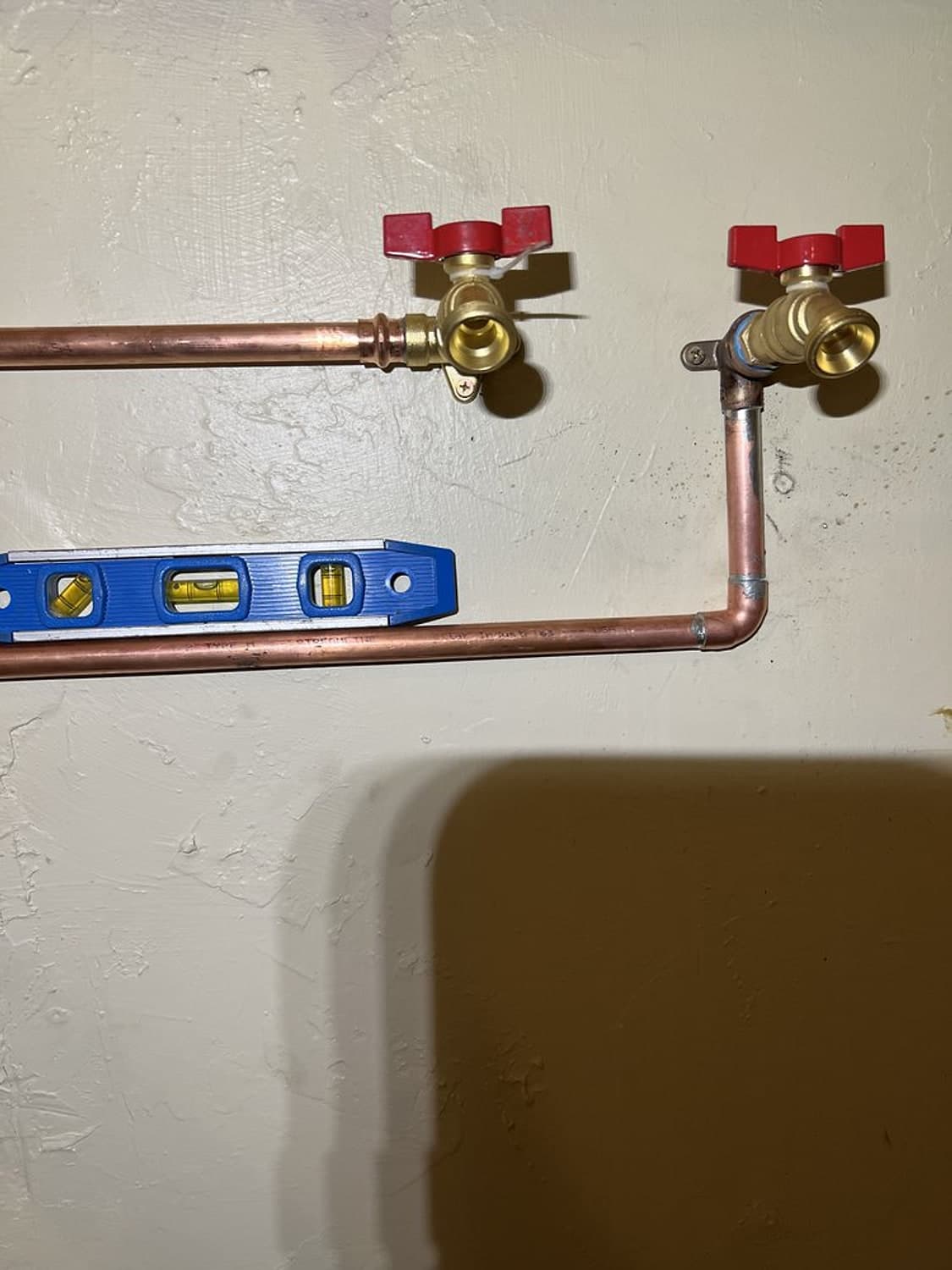 New copper hot and cold water lines with red-handled valves, checked with a blue level on a white wall