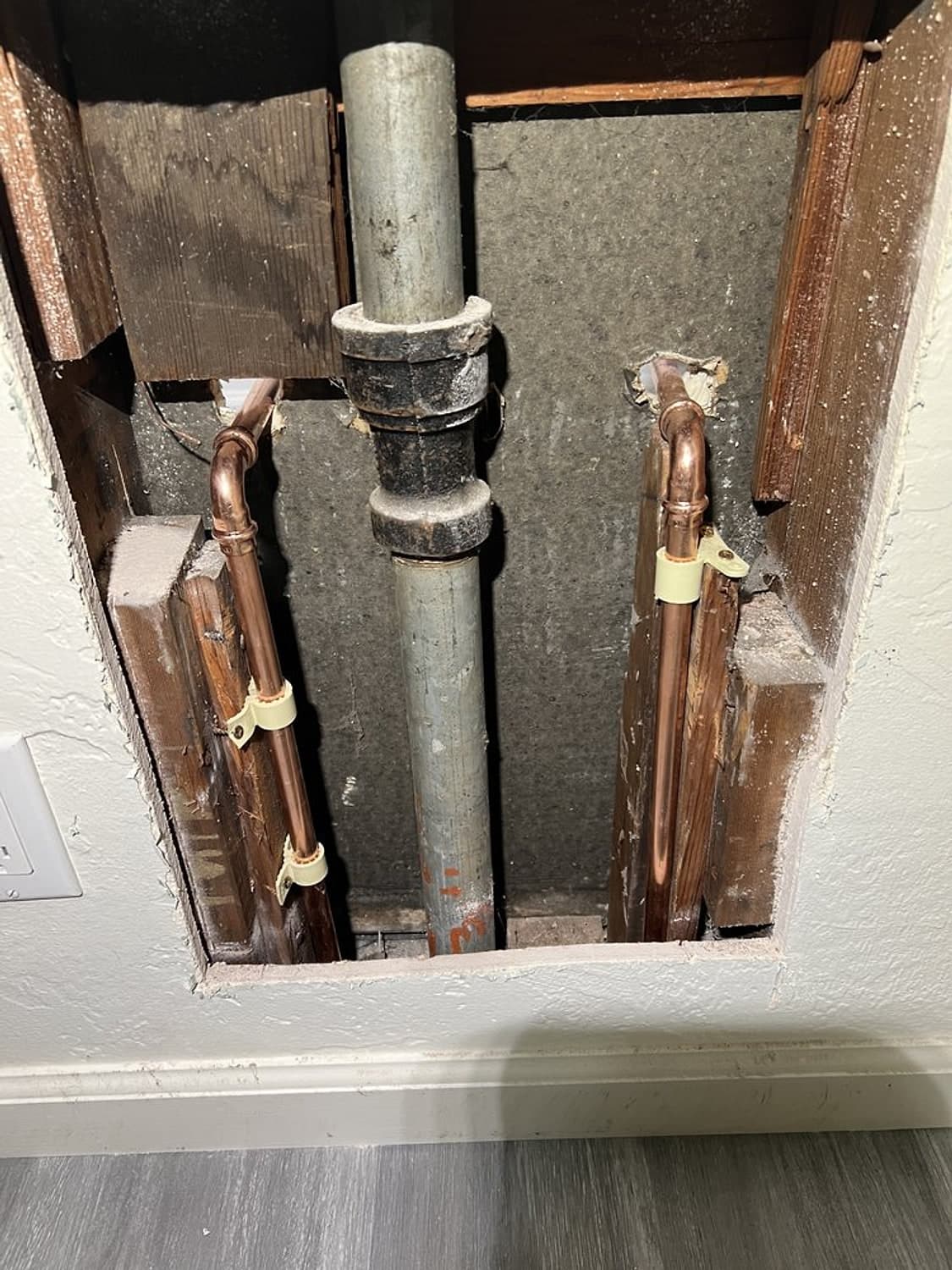 New copper water lines inside an opened wall beside an old gray pipe