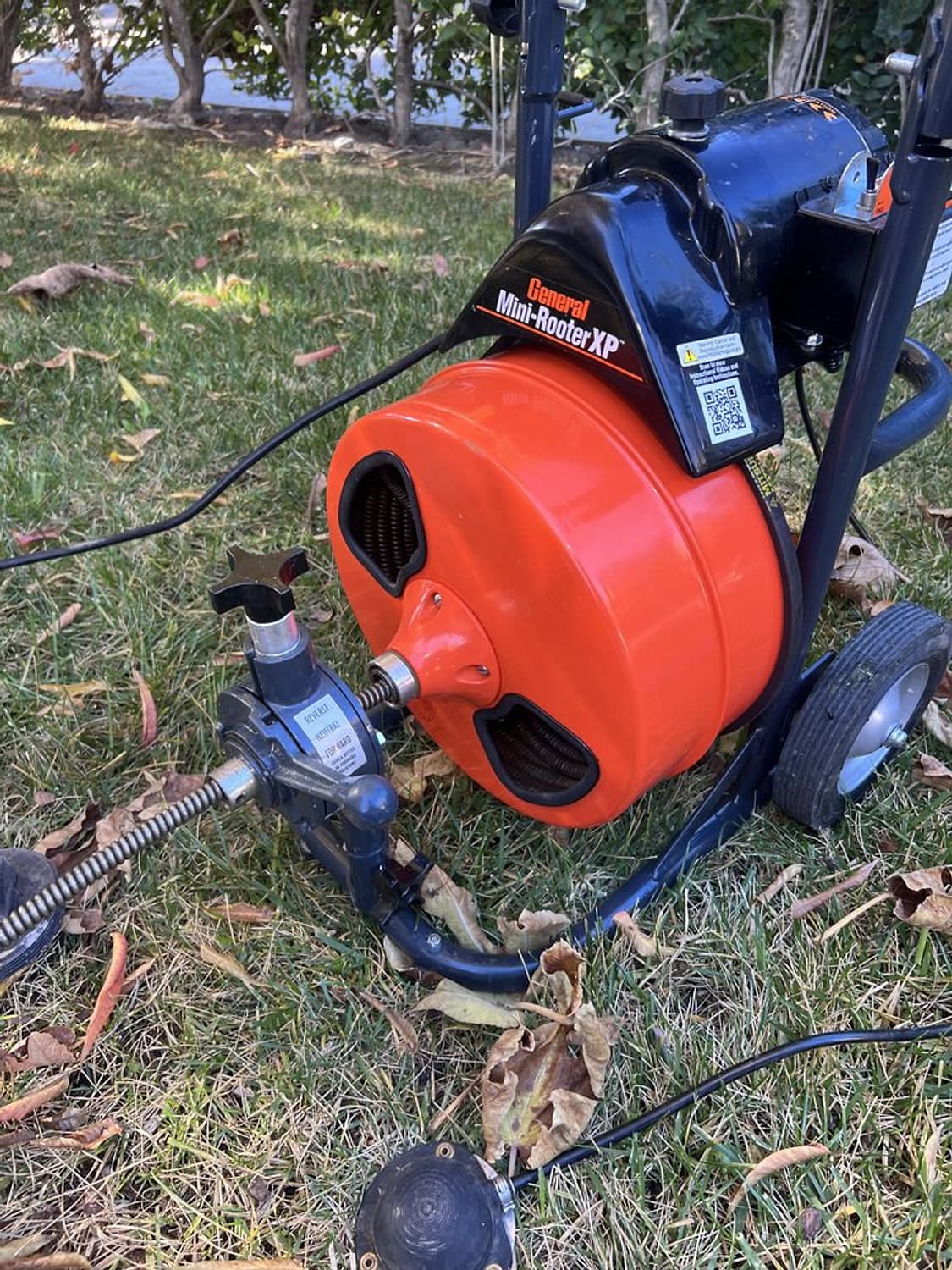 Red drain cleaning machine on the grass with its cable fed into an outdoor cleanout