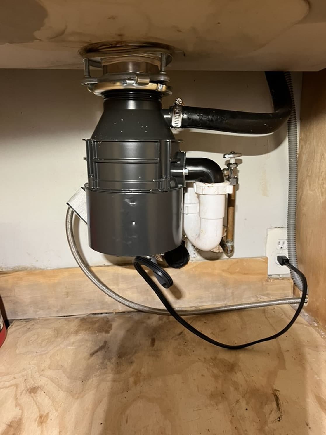 New gray garbage disposal and drain connections under a kitchen sink