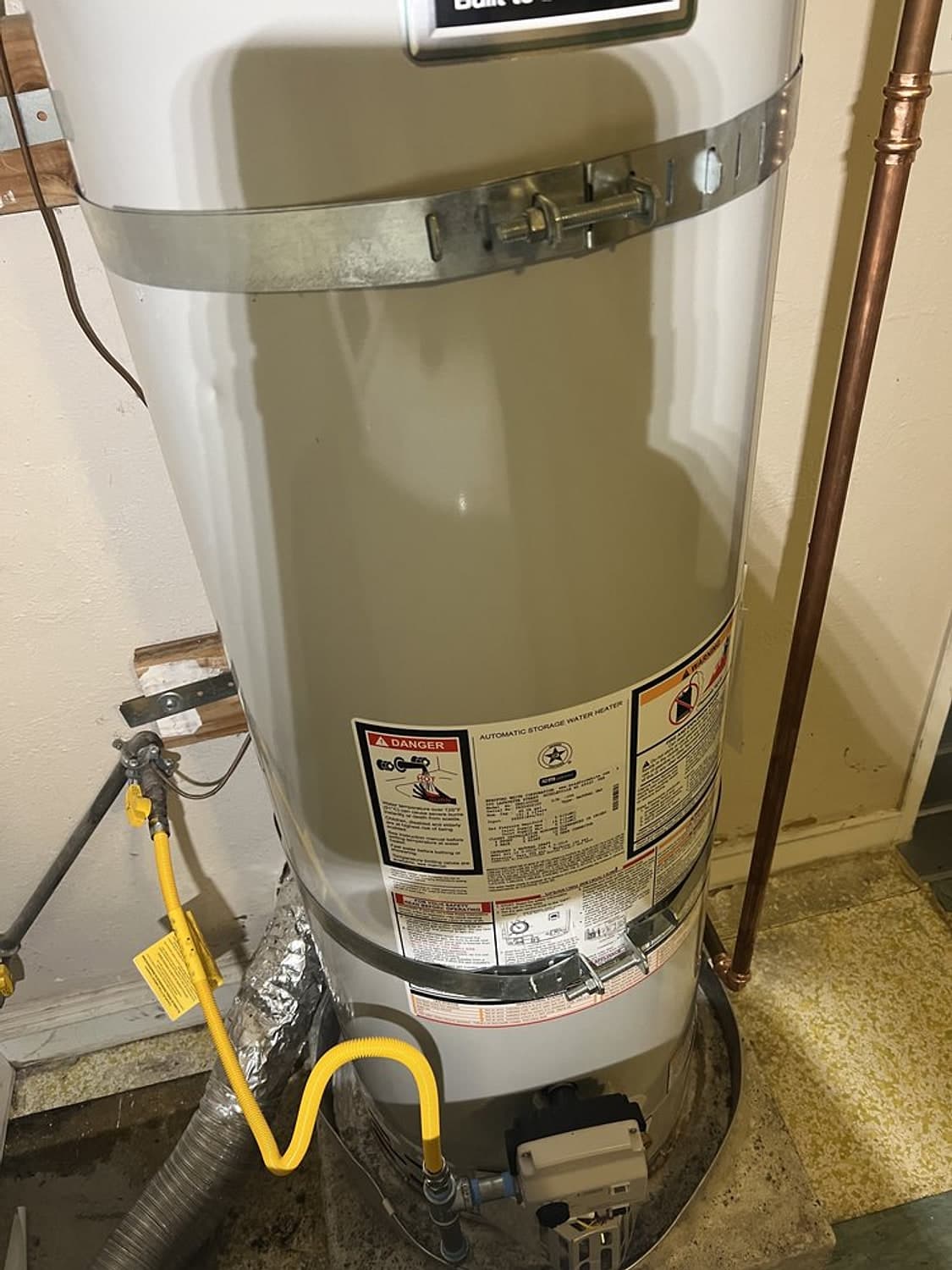 New yellow flexible gas line and shutoff valve running to a Bradford White water heater with seismic straps