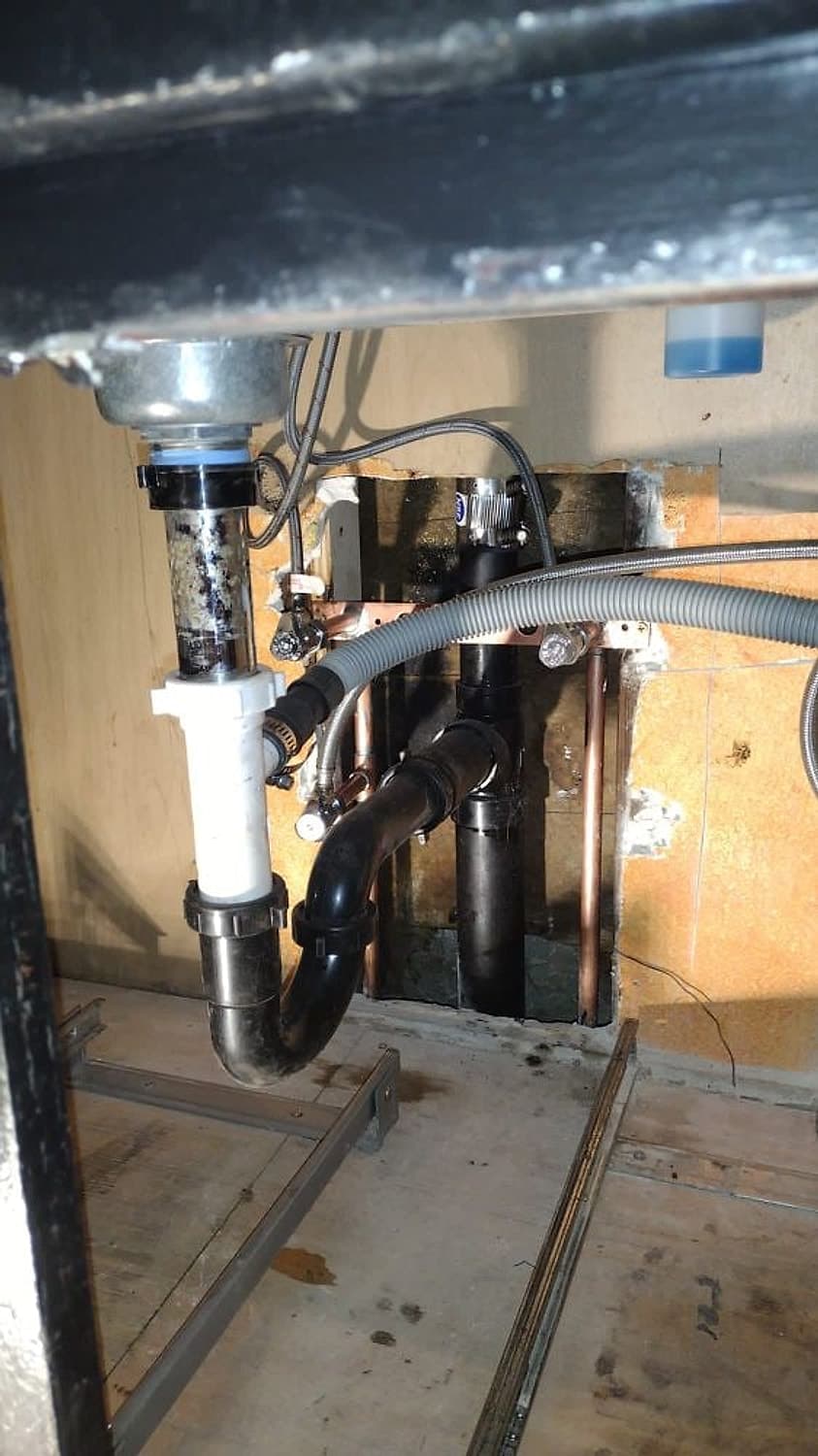 Under-sink view of a new drain trap and garbage disposal connection with copper supply lines