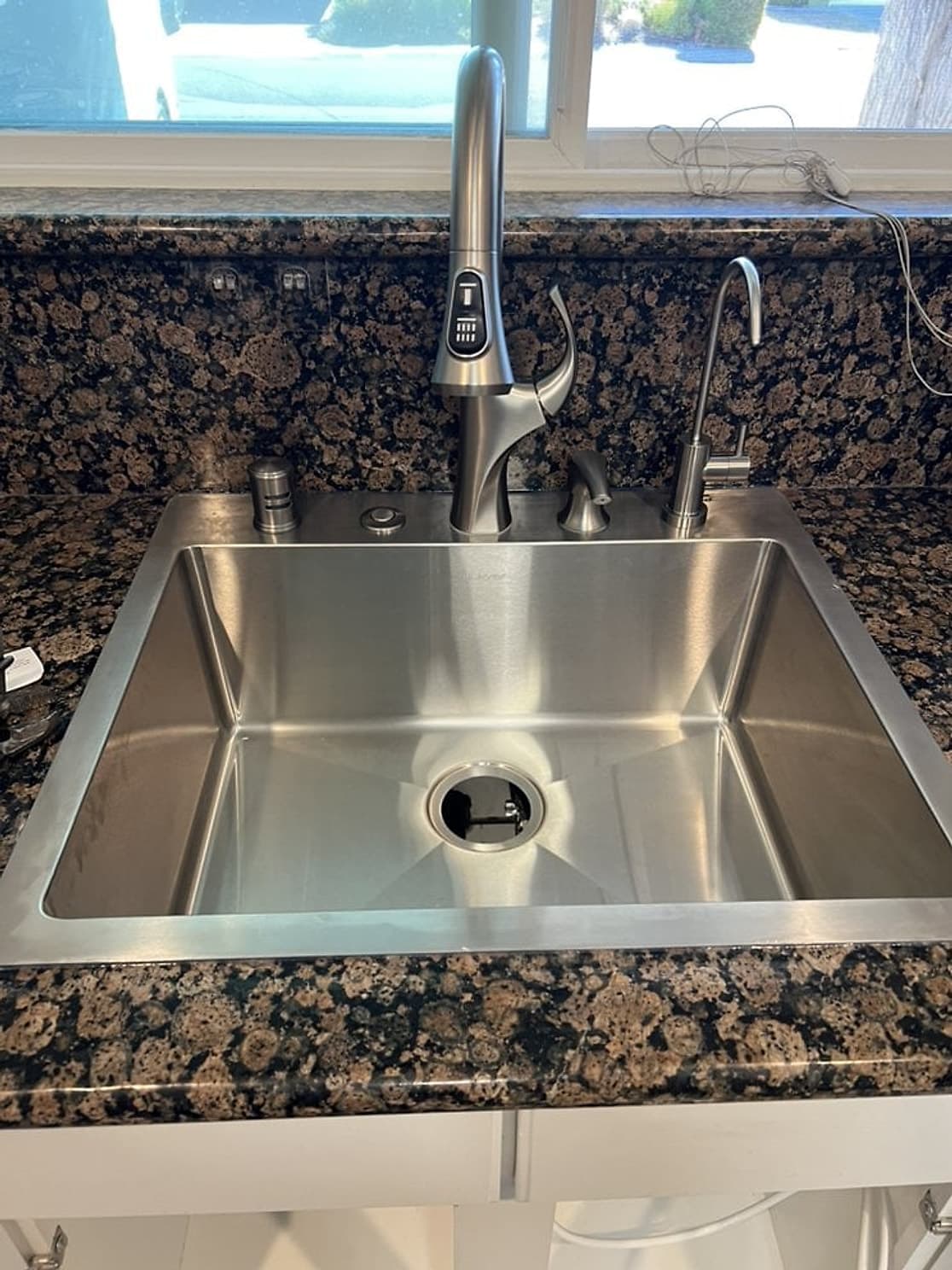 Fregadero nuevo de acero inoxidable con llave extraíble y una llave aparte para agua filtrada en una cubierta de granito