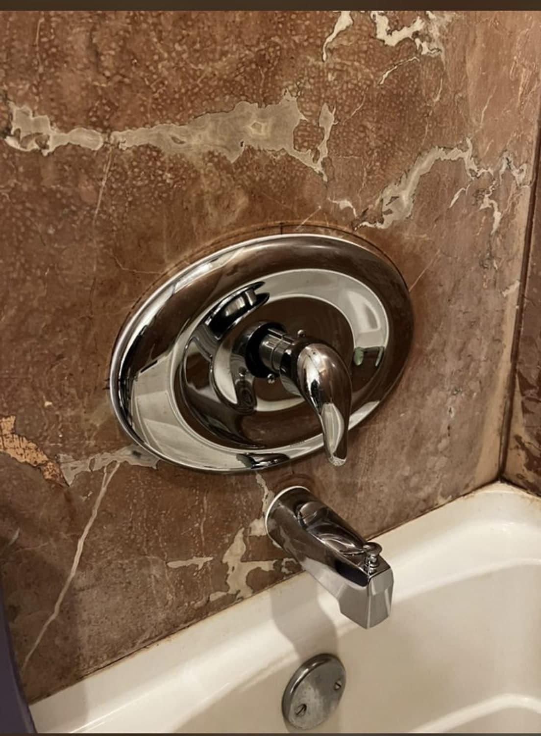 New chrome Moen shower valve handle and tub spout on brown marble tile