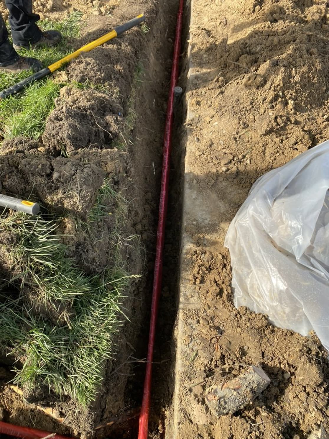 A new red-sleeved main water line laid in a narrow trench through a lawn