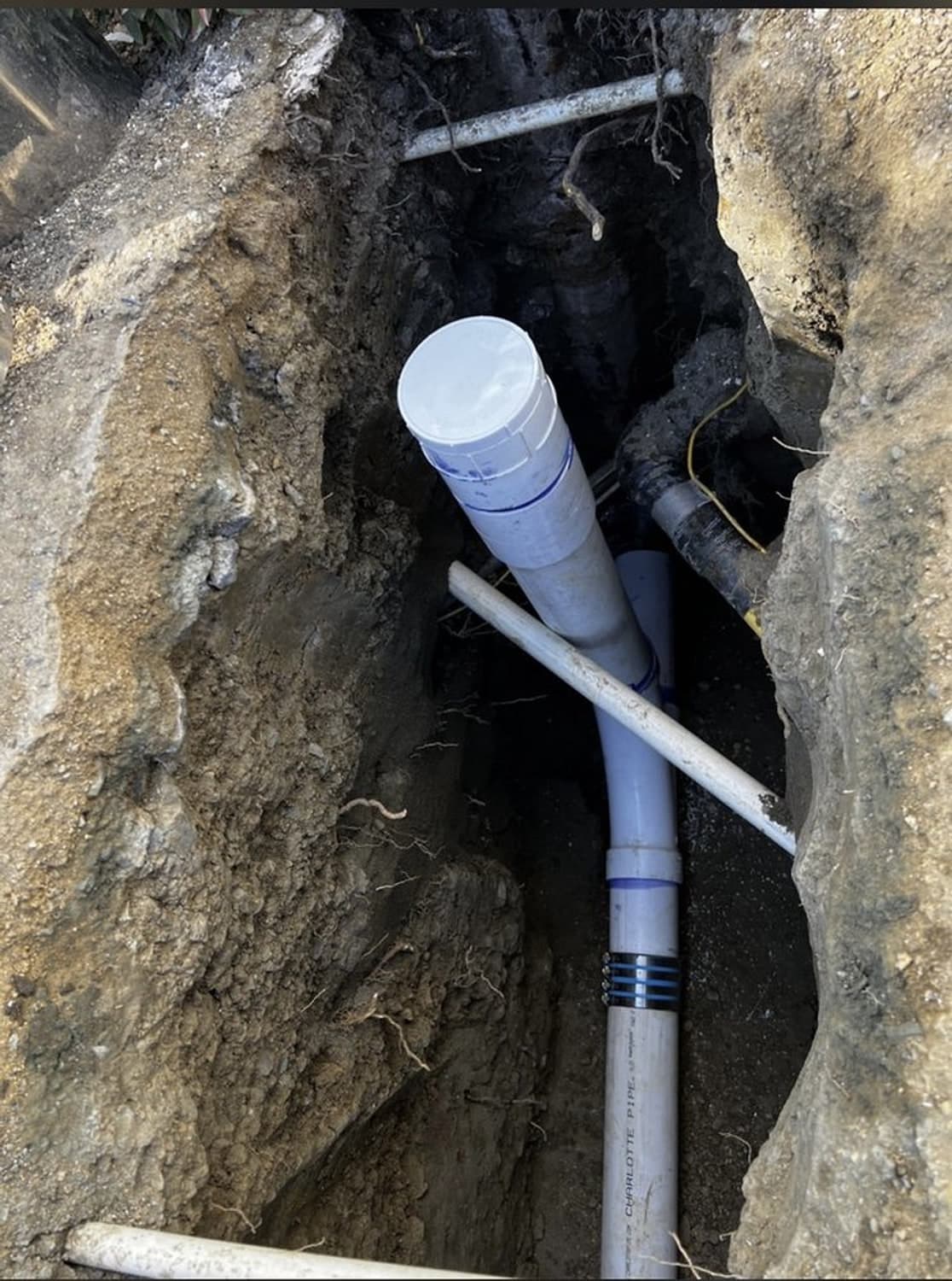 New white sewer pipe and fittings set in a deep open trench, before backfill