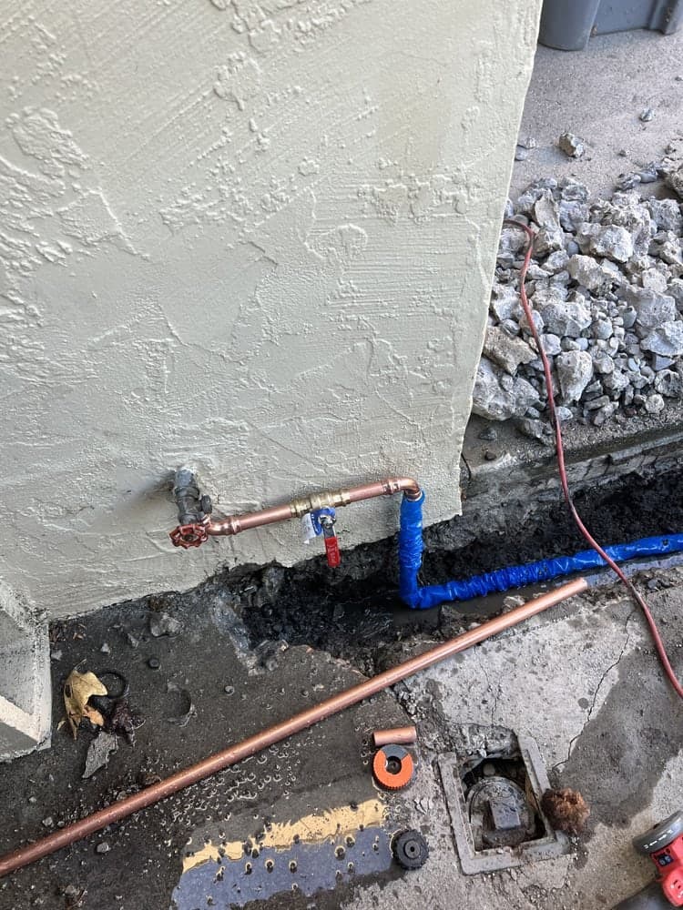 New copper and blue water line running along a stucco wall to an outdoor faucet, with a shallow trench