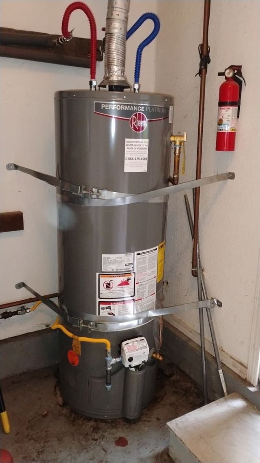 New 50-gallon Rheem gas water heater with seismic straps, a new vent and a yellow gas line in a garage corner
