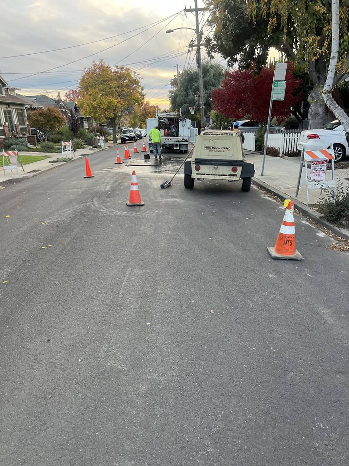 A residential street coned off around a work area, with a work truck and a compressor parked on the road