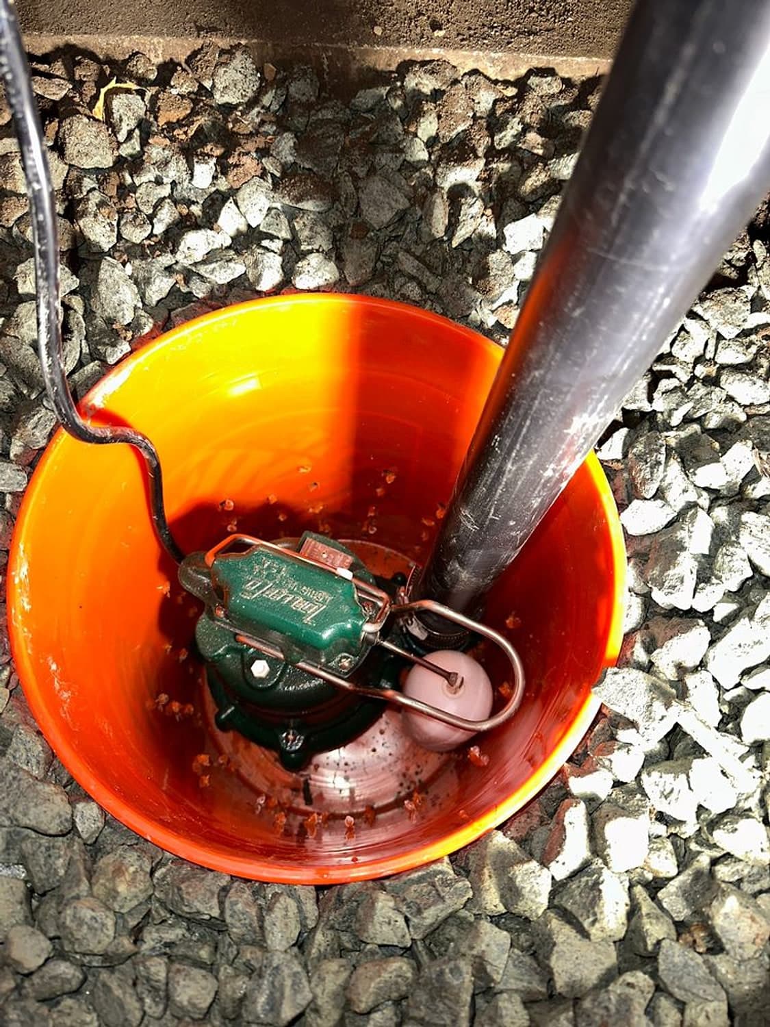 New sump pump sitting in an orange basin set into gravel, with its discharge pipe