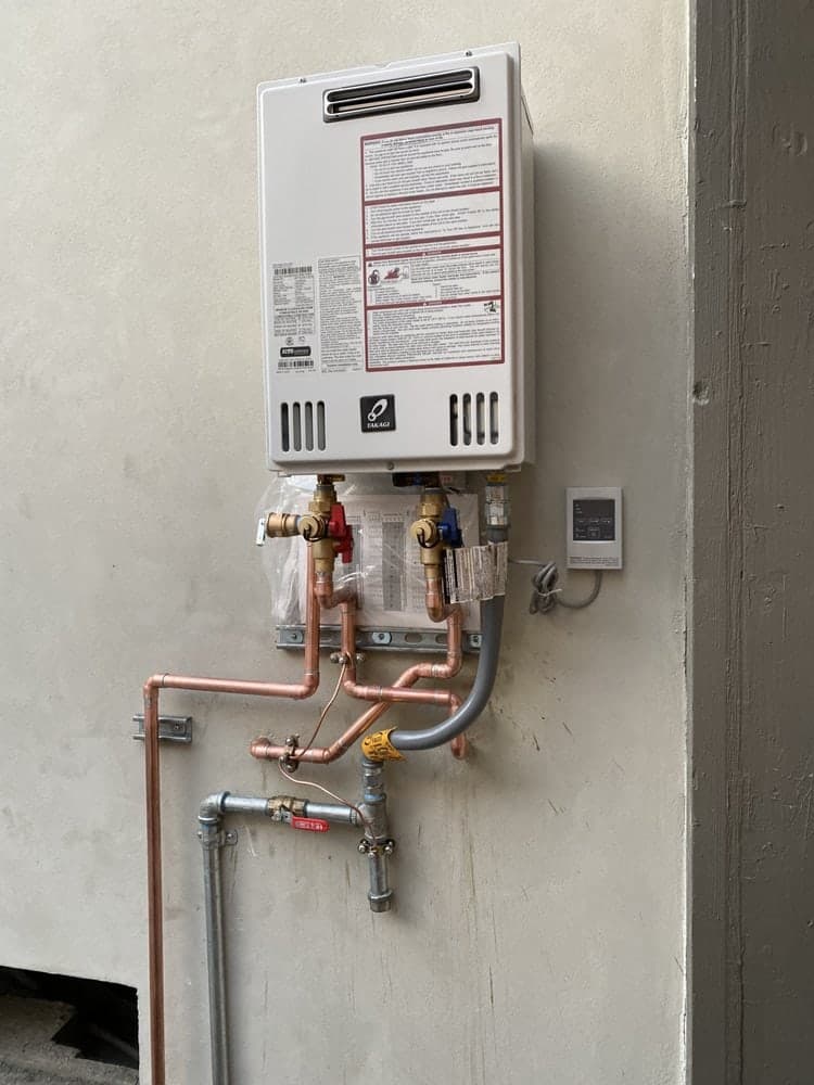 Tankless water heater mounted on a garage wall with copper piping and red and blue service valves