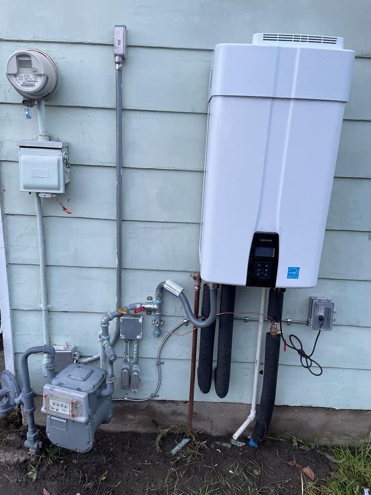 White tankless water heater on blue siding next to a gas meter and electrical panel