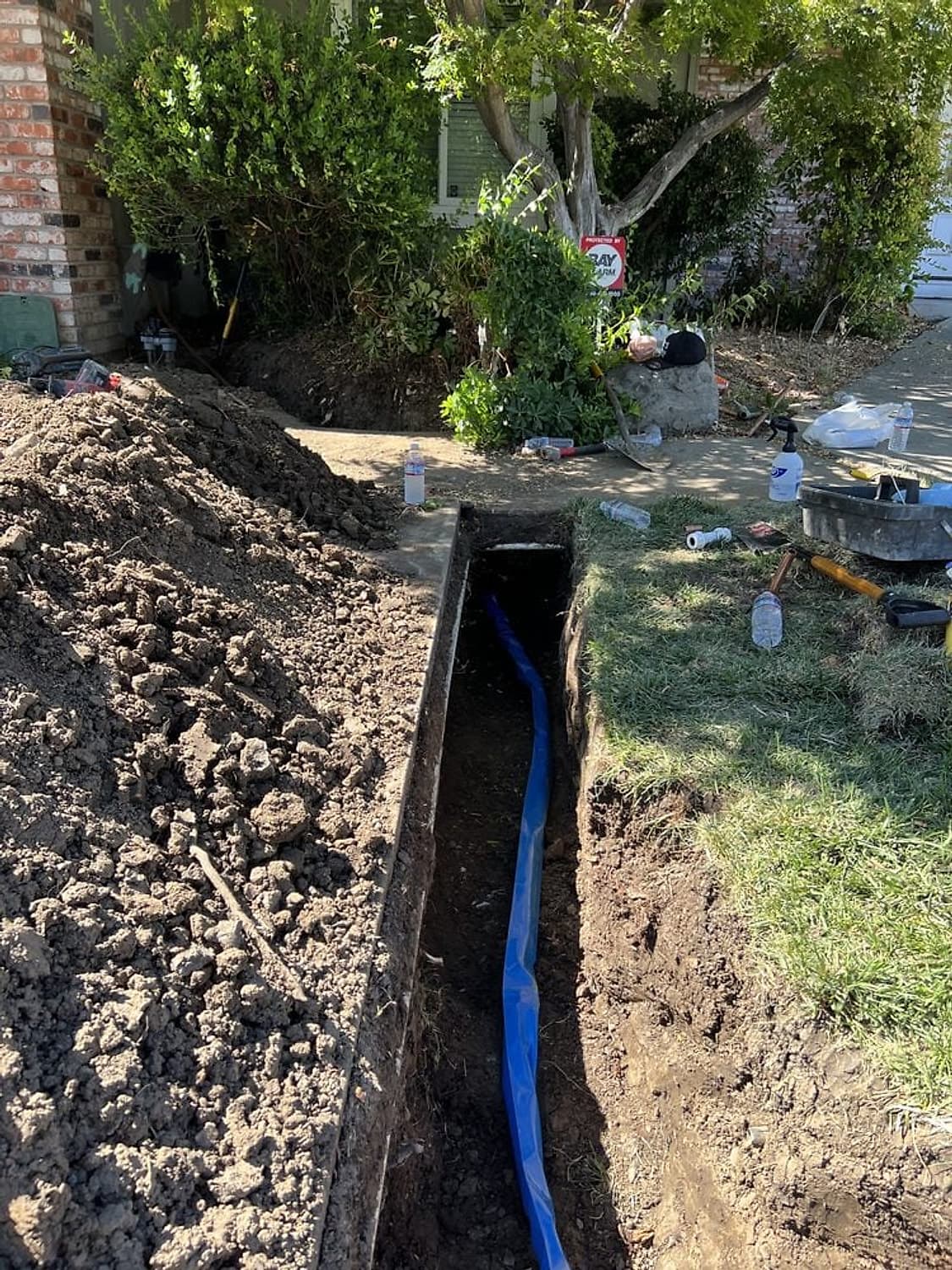 Narrow trench across a front yard with a new blue water service line laid at the bottom