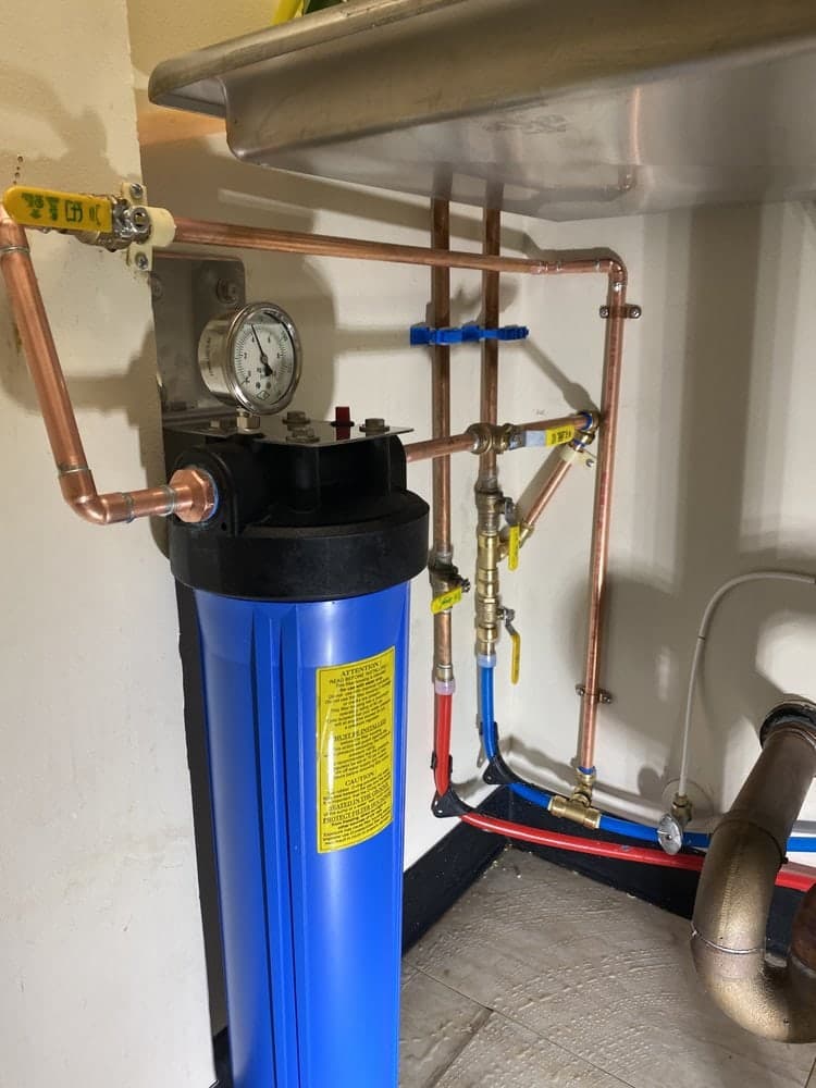 Blue whole-house water filter housing with a pressure gauge and copper bypass valves